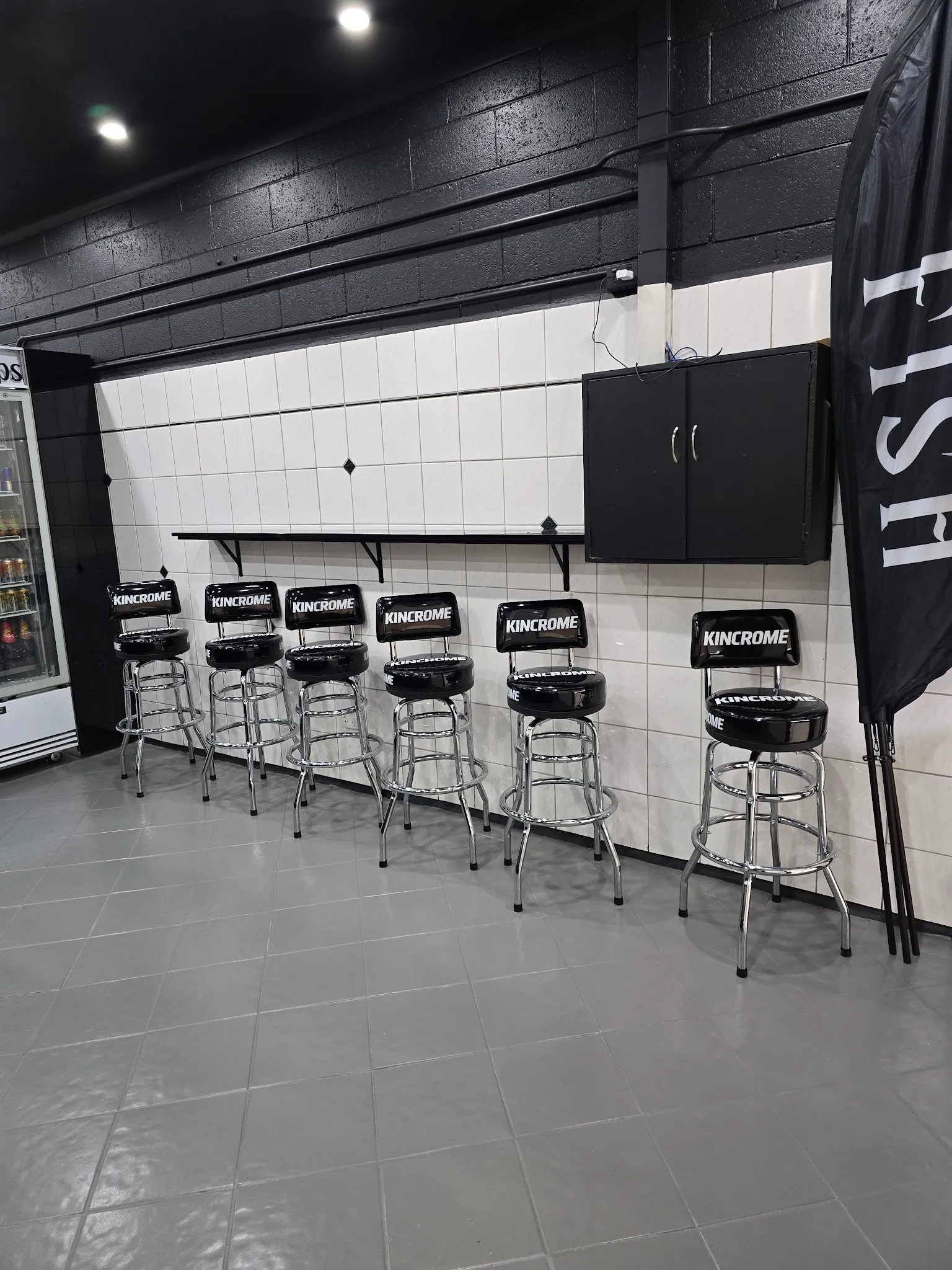 Black bar stools against the white-tiled wall inside the shop