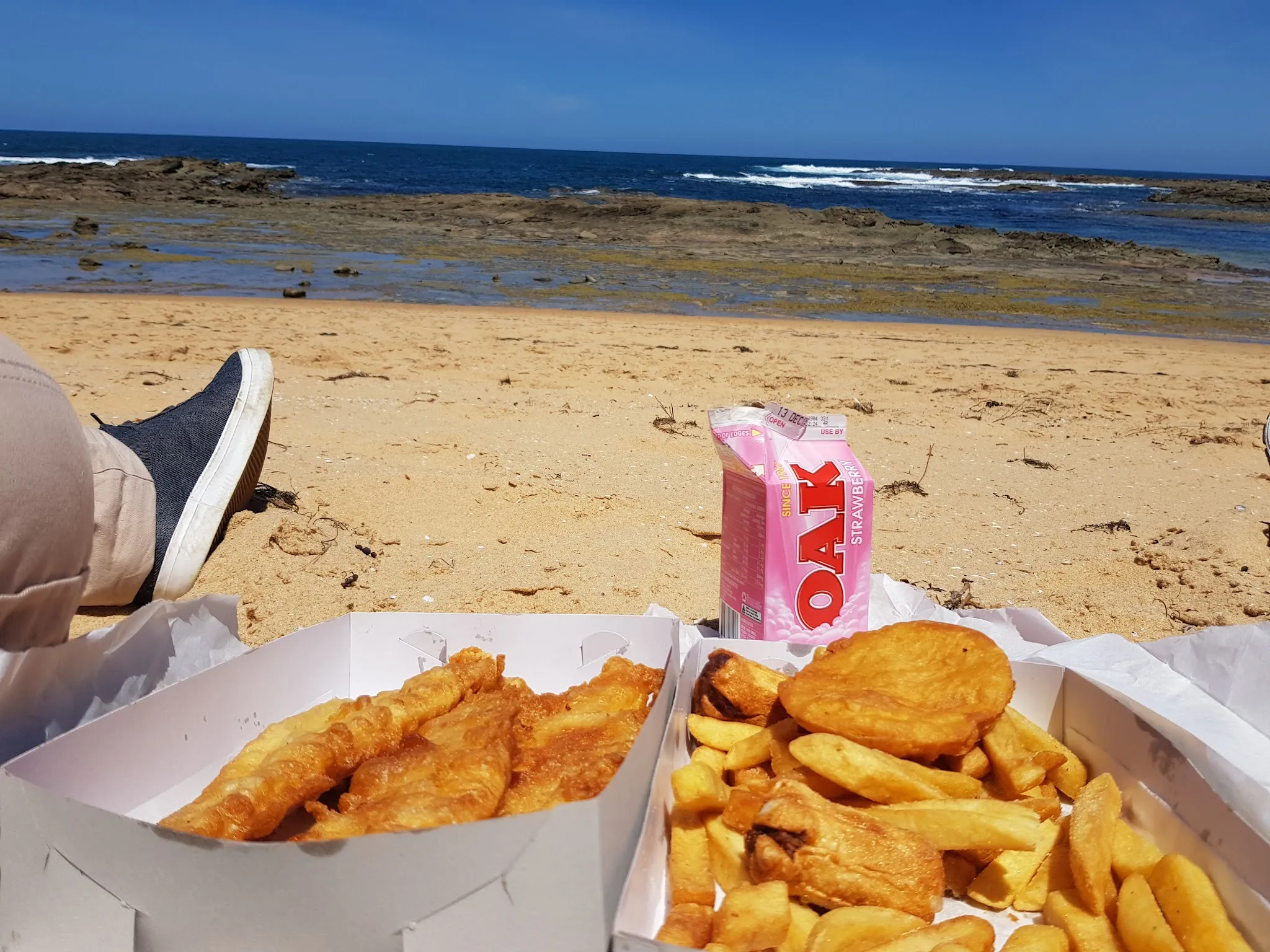 Fish and chips in takeaway boxes on the beach at Grantville with the bay behind